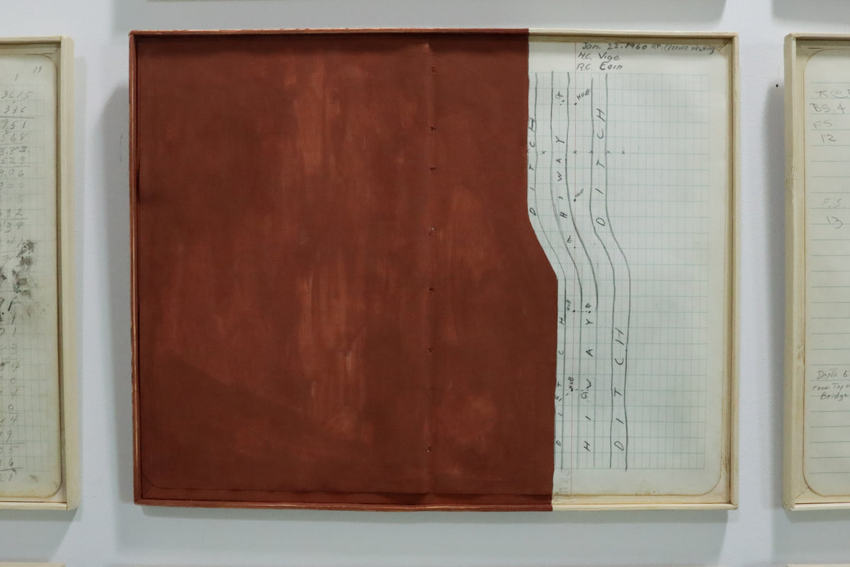 A framed abstract artwork hanging on a white wall, featuring a large reddish-brown rectangular panel on the left and a right panel with handwritten mathematical or scientific notes on graph paper.